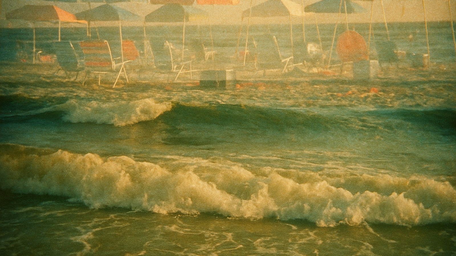 Vintage film photo of ocean waves with double exposed beach umbrellas and chairs floating like ghosts above the water, showing permanent natural cycles overlaid with temporary structures