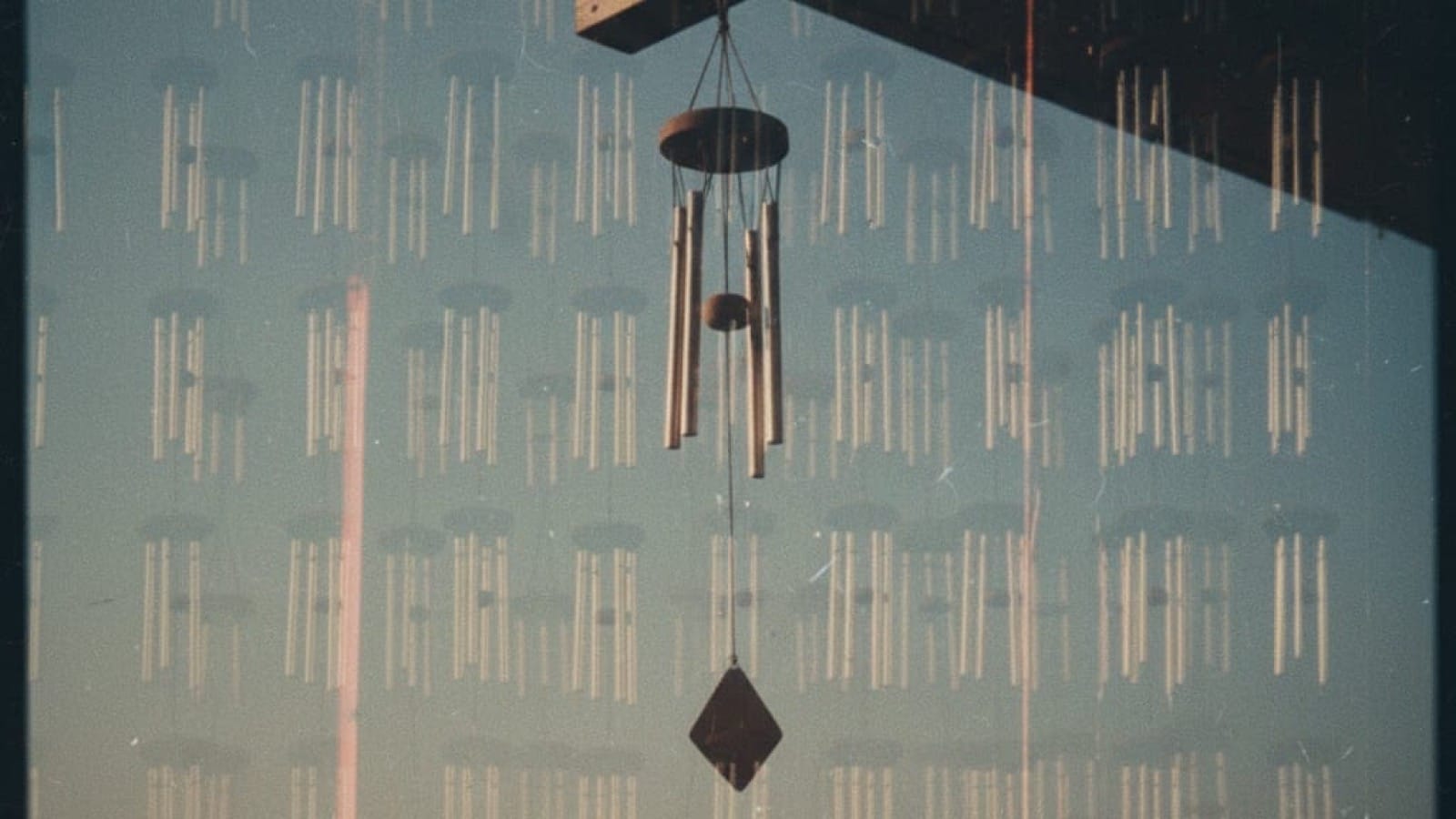 Vintage film photo: single wind chime with ghostly overlay of hundreds of identical chimes creating visual static, showing how optimization becomes noise through repetition