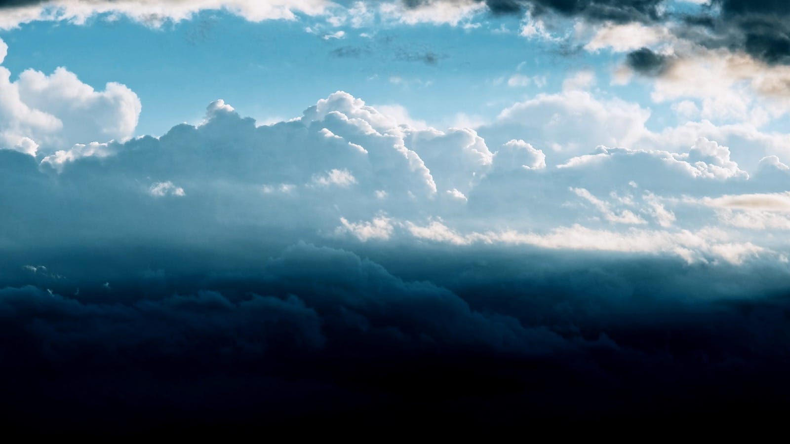 Dramatic cloudscape showing dark turbulent clouds below and bright illuminated clouds above blue sky, representing fragmented campaign execution below unified governance frameworks above
