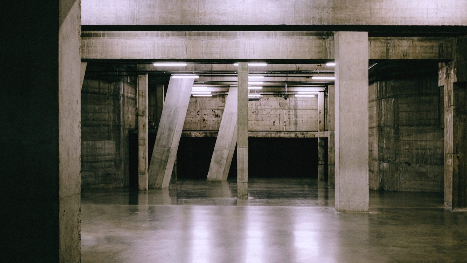 A stark, brutalist concrete interior with massive industrial pillars and fluorescent overhead lighting, representing the cold, functional reality of sovereign compute infrastructure.