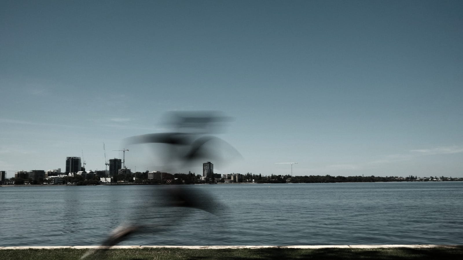 Blurred figure in motion along waterfront with static cityscape in background, representing finite sprint engagements versus permanent infrastructure built.