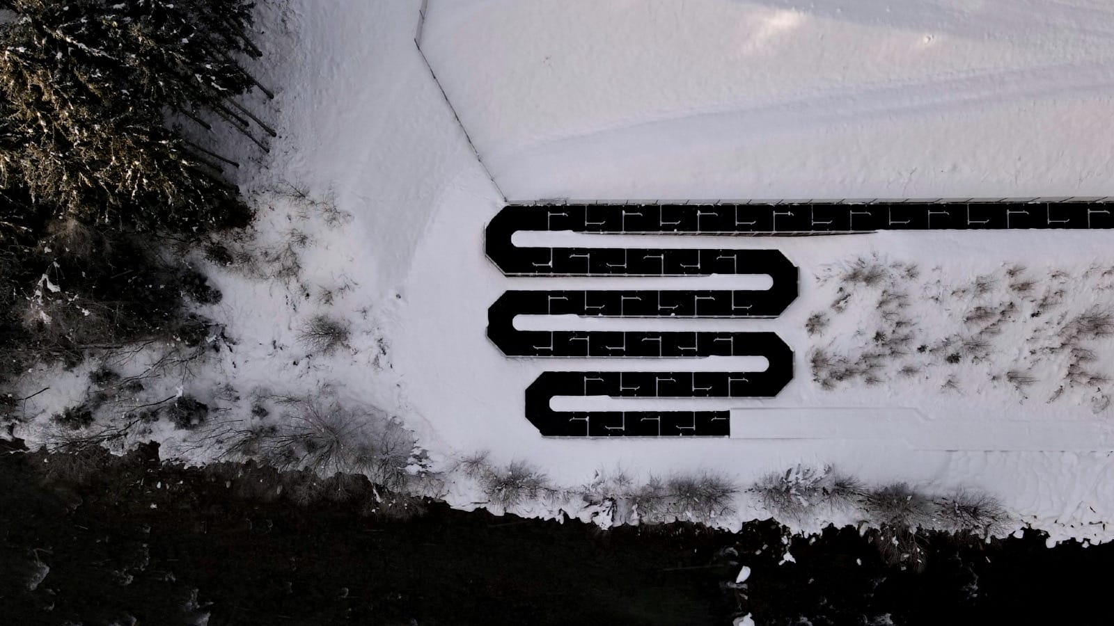 Aerial view of a snow-covered winding road through a dark forest