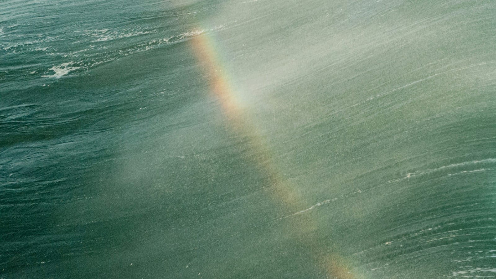 Rainbow forming in ocean spray over green surf