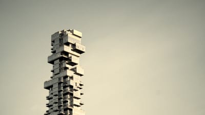 Staggered modular concrete blocks of a brutalist skyscraper against a desaturated sky. A metaphor for structural coherence in modular content architecture.