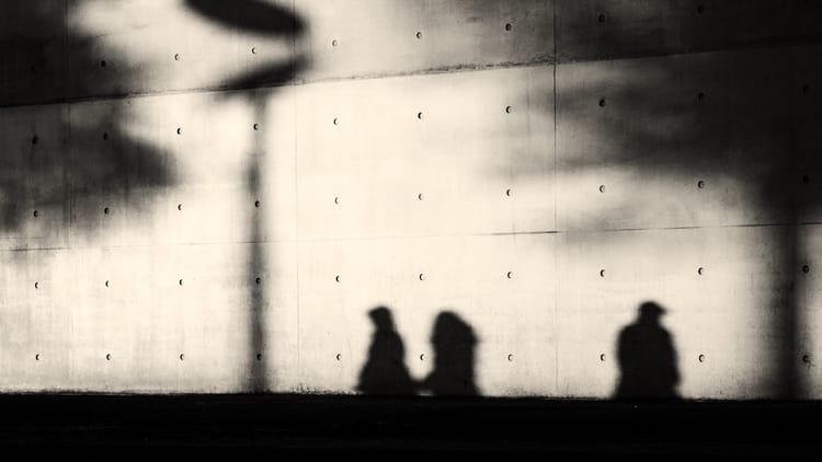 Abstract black and white photograph showing silhouetted figures against textured concrete wall with dramatic shadows, representing fragmented brand identity across multiple touchpoints